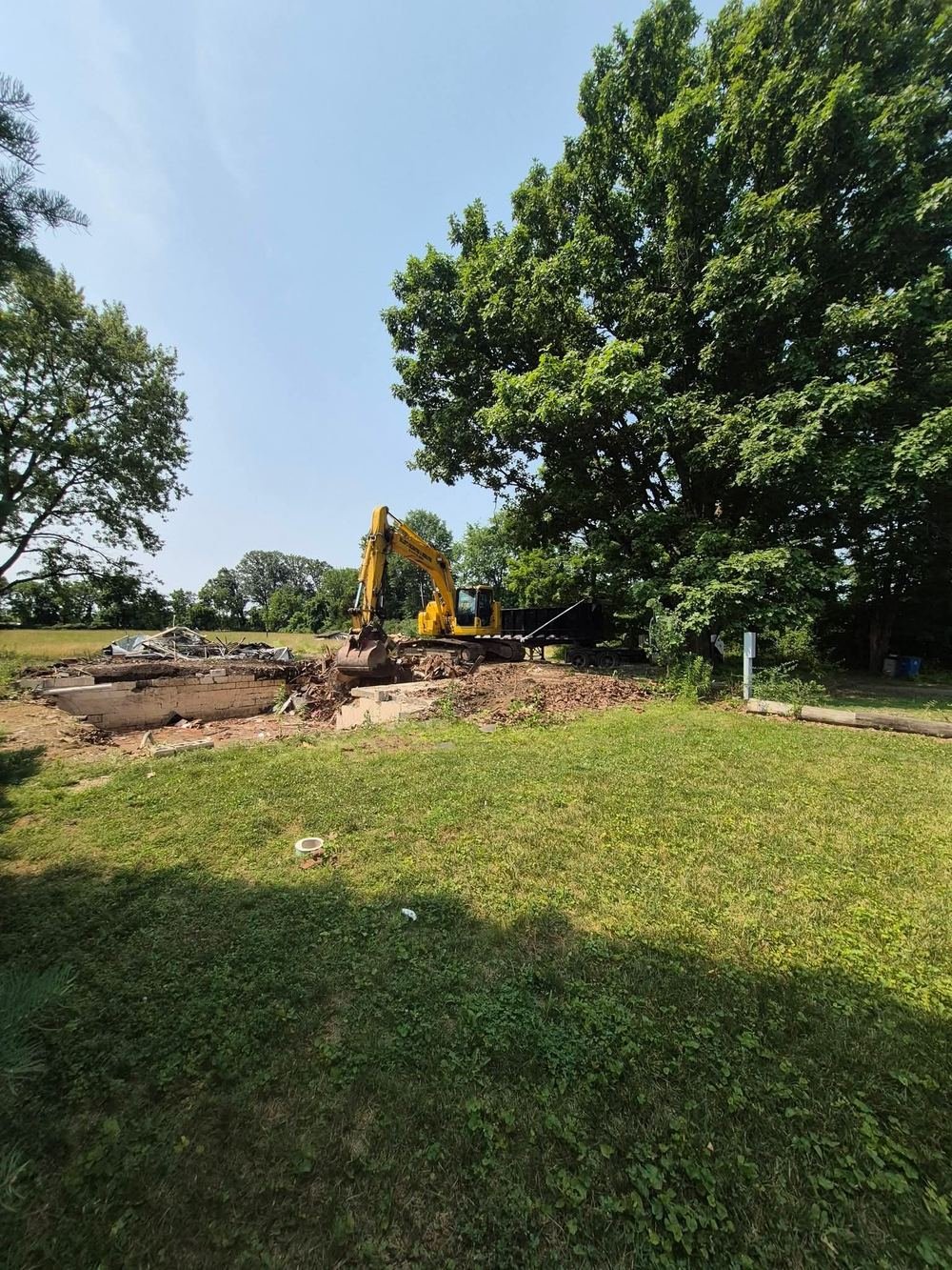 Excavator breaking out a block foundation with a dump trailer behind it